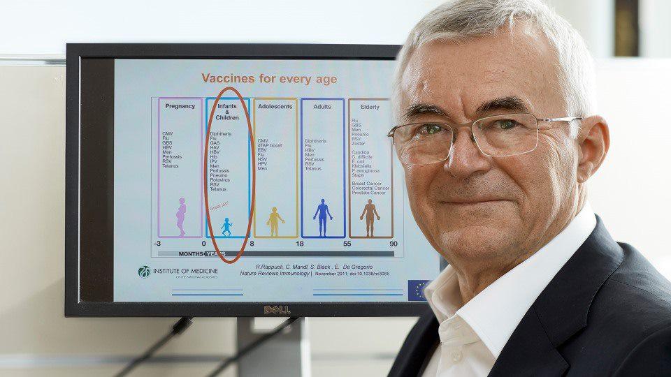 Erfinder lächelt vor einem Bildschirm, auf dem Informationen über Impfstoffe angezeigt werden
